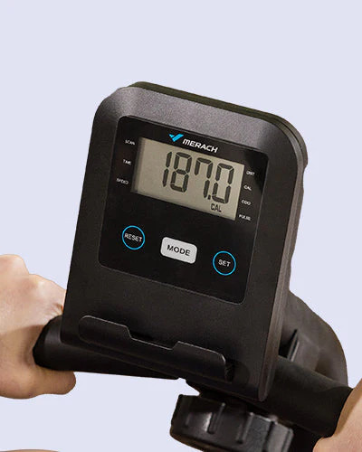 Primer plano del monitor LCD de la bicicleta Merach mostrando el contador de calorías (187.0 CAL) y botones de control Reset, Mode y Set para seguimiento de velocidad, tiempo y distancia